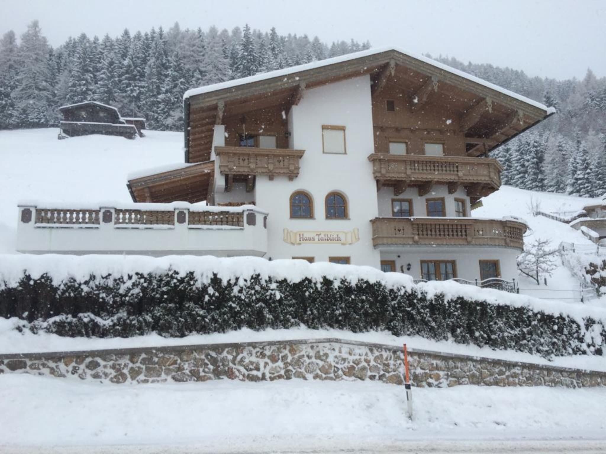 Un chalet à plusieurs étages, doté de balcons et entouré d’arbres couverts de neige.