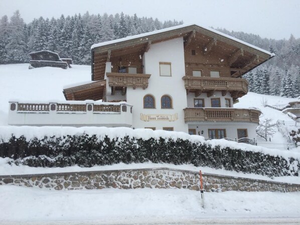 A multi-story chalet with balconies, surrounded by snow-covered trees.