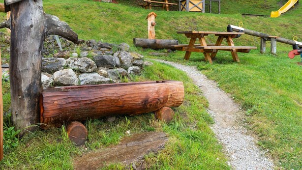 A park with a wooden log structure, picnic tables, a yellow slide, and a small birdhouse. - Apartment in Hainzenberg near Ski Lift (Hainzenberg)