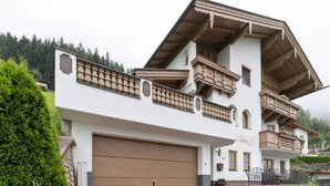 A two-story building with a large garage door, balconies with intricate railings, and a mountainous backdrop. - Apartment in Hainzenberg near Ski Lift (Hainzenberg)