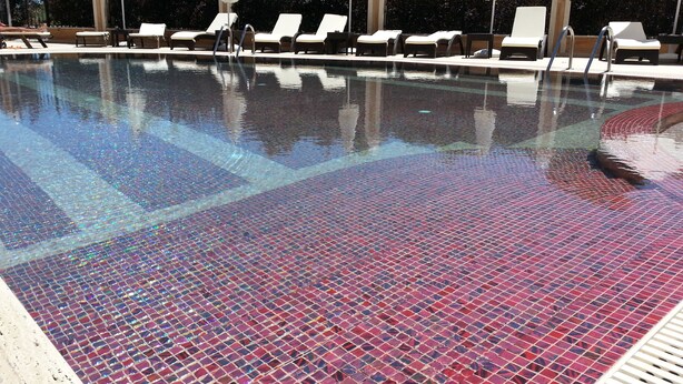 A swimming pool with a tiled floor, surrounded by lounge chairs and umbrellas. - River Park - Menada Apartments (Sunny Beach)