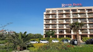 A multi-story hotel named River Park with balconies, a parking lot, and surrounding greenery. - River Park - Menada Apartments (Sunny Beach)