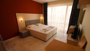 A hotel room with a large bed, a wooden desk, a television, and a window with curtains. - River Park - Menada Apartments (Sunny Beach)