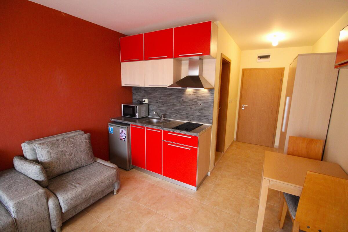 A compact kitchen with red and white cabinets, a built-in microwave, and a small dining area with a wooden table and chairs.