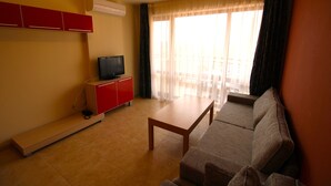 A living room with a sofa, a coffee table, a TV on a stand, and a window with curtains. - River Park - Menada Apartments (Sunny Beach)