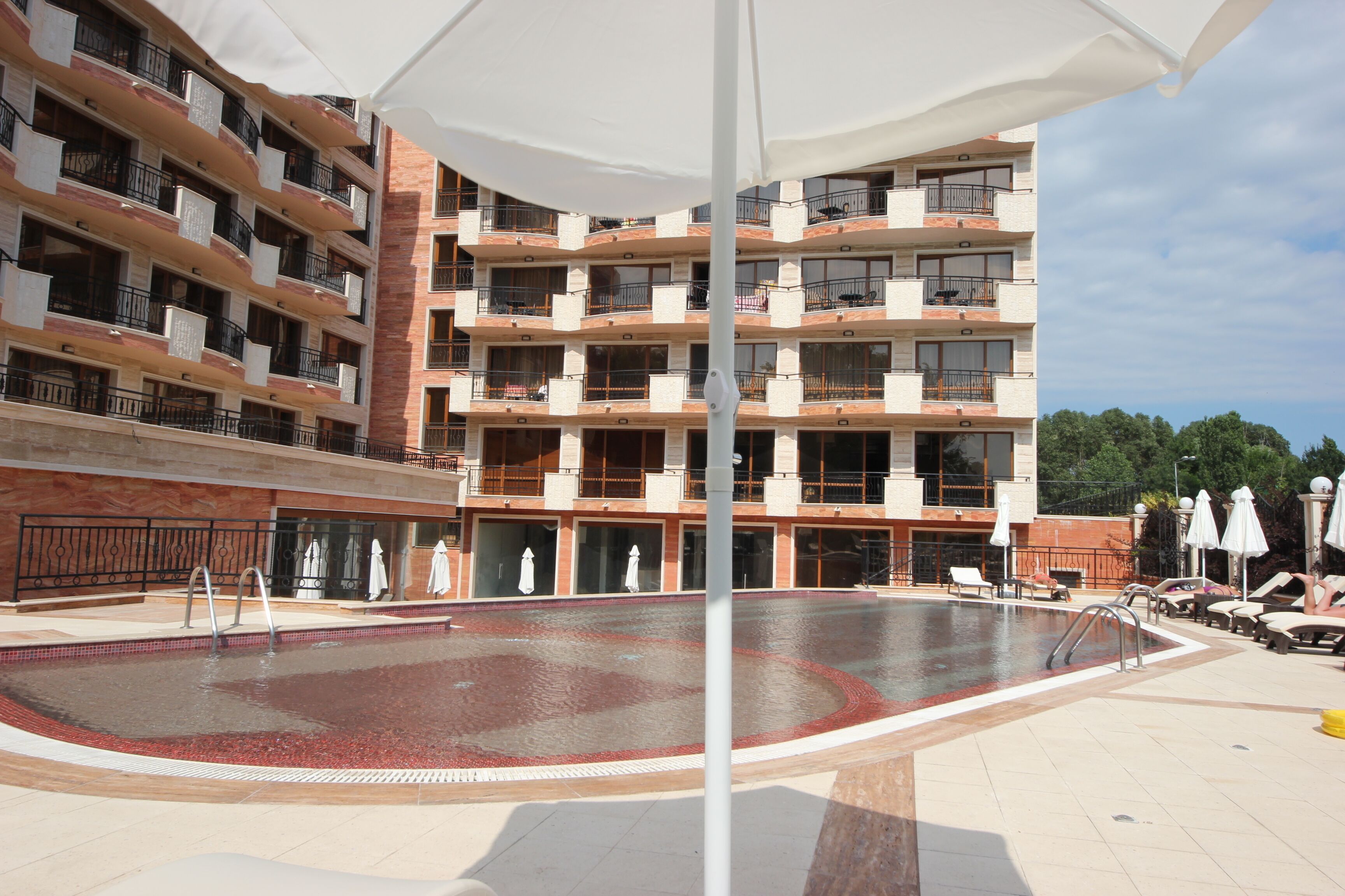 Um hotel com vários andares, piscina, área de estar externa e espaço coberto com guarda-sóis.