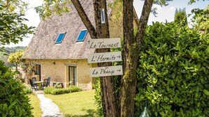 Une maison de campagne en pierre, avec un toit de chaume, un panneau indicateur en bois muni de flèches directionnelles et un sentier menant à la maison.