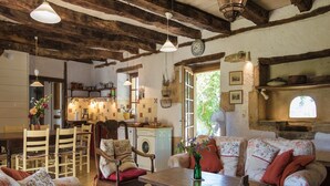 Une cuisine rustique avec des poutres en bois, un coin repas avec des meubles à motifs floraux et un salon confortable avec un canapé et une table.