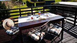 An outdoor dining area with a table set for four, surrounded by wooden chairs with plaid cushions.