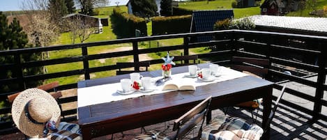 An outdoor dining area with a table set for four, surrounded by wooden chairs with plaid cushions.