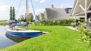 Un canal où est amarré un bateau bleu, sur une pelouse, entouré de maisons aux toits inclinés, sous un ciel dégagé.