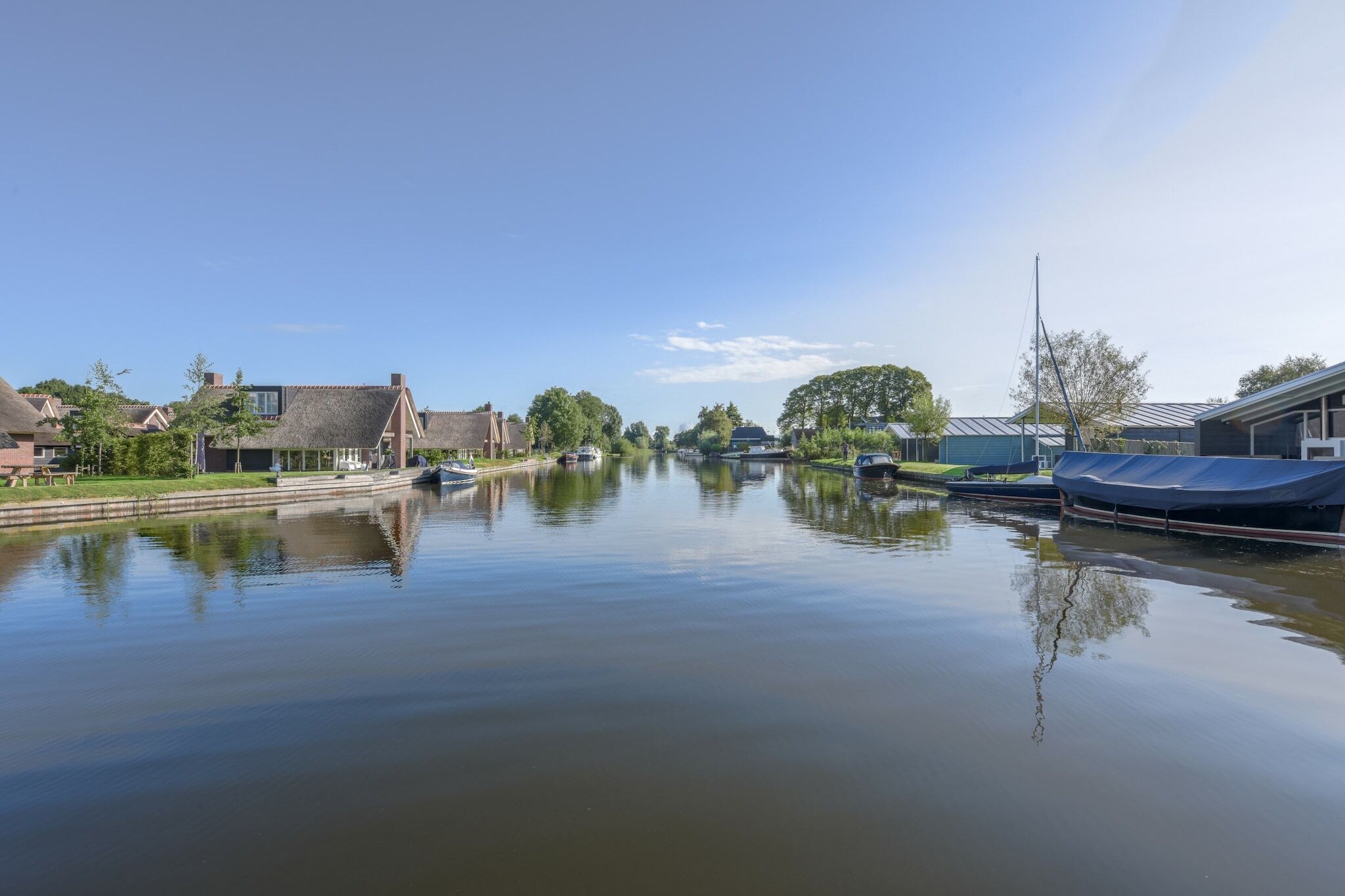 Une rivière paisible, bordée de bateaux, de maisons et d’arbres.