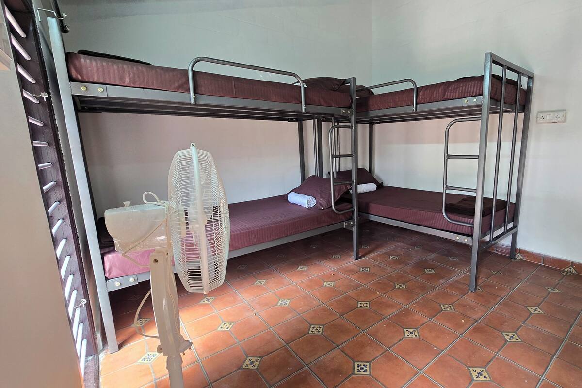 Ein Schlafsaalzimmer mit Etagenbetten, einem Standventilator und einem Fliesenboden.