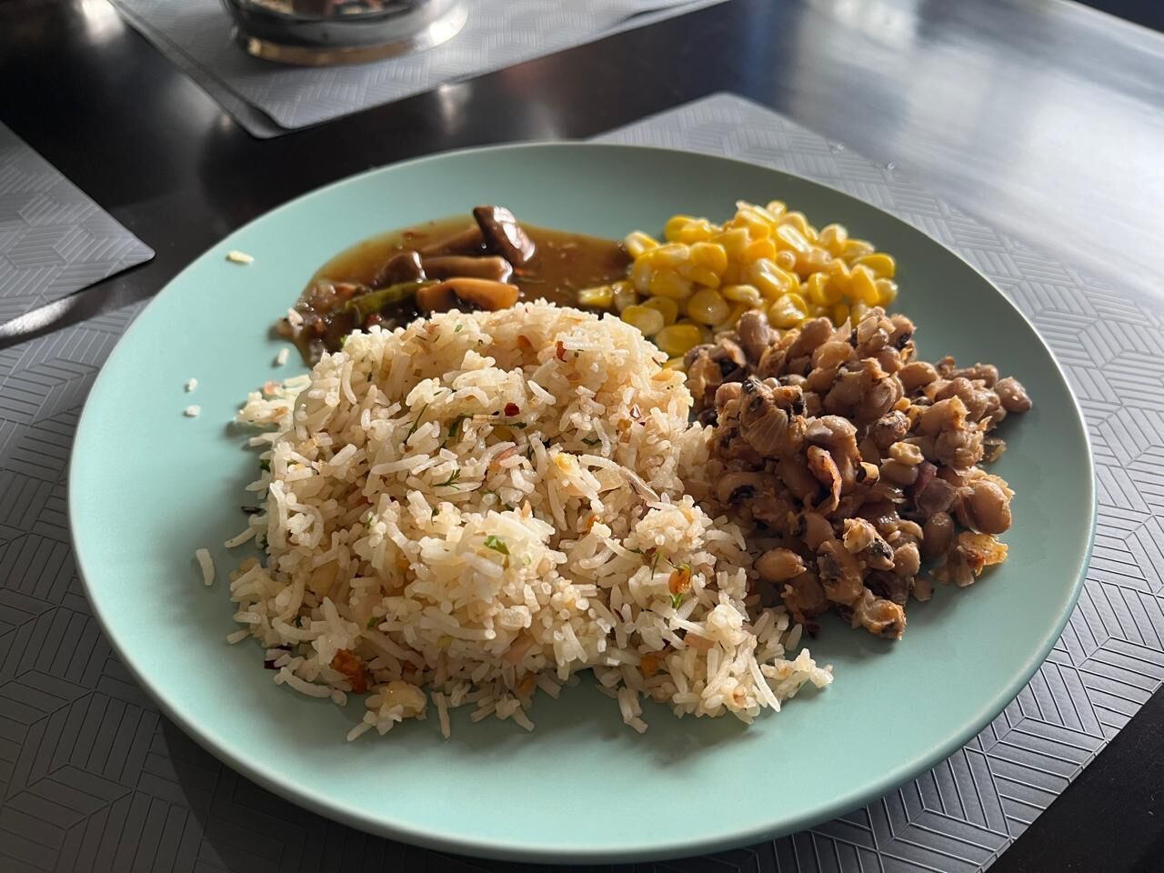 Un plato de comida con arroz, frijoles y maíz sobre una mesa.
