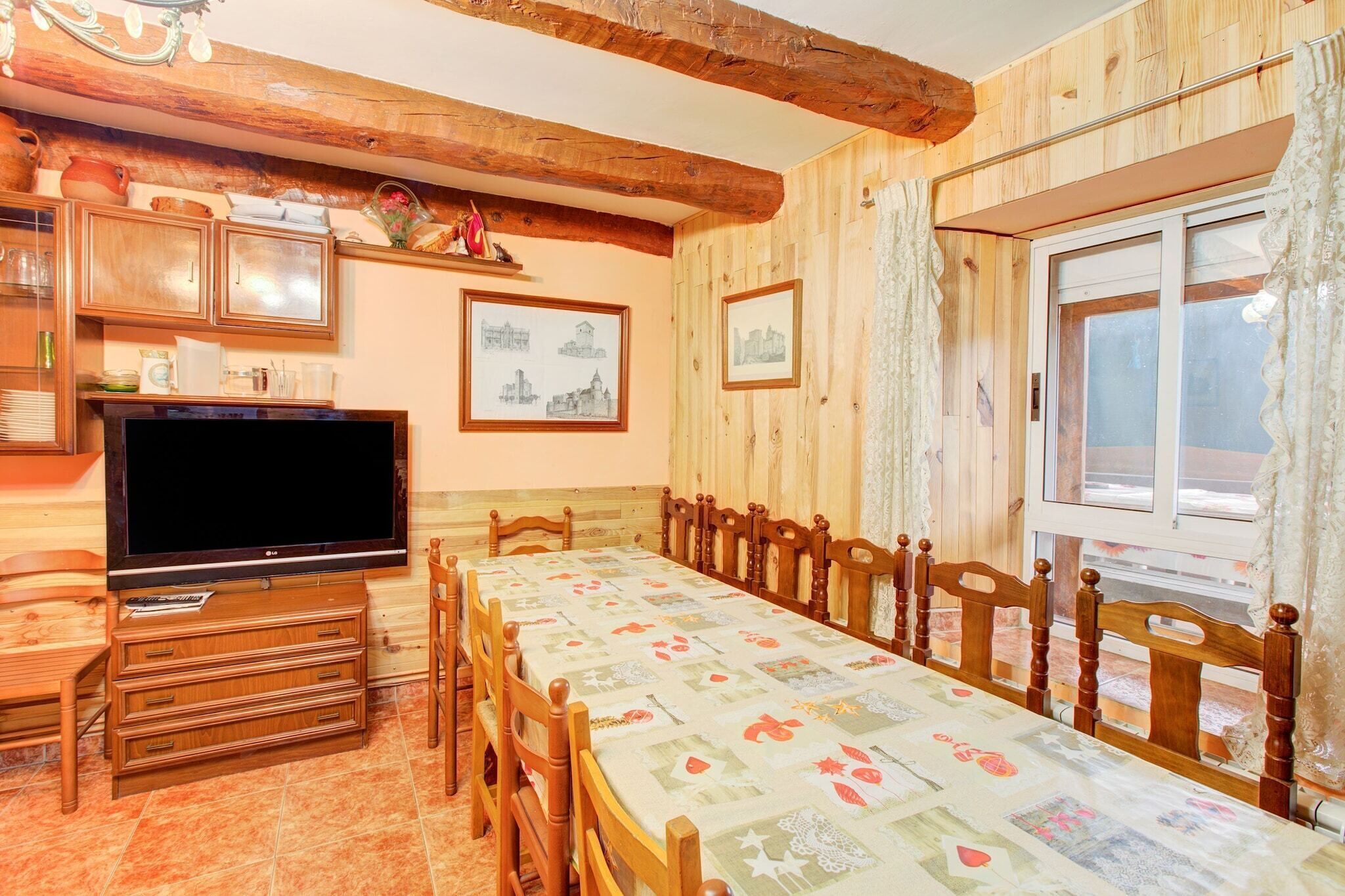 Une salle à manger avec une longue table en bois, des chaises, un téléviseur, des meubles en bois et des tableaux encadrés accrochés au mur.