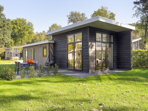 Een modern huis met een terras, een hangstoel en een tafel met pompoenen.