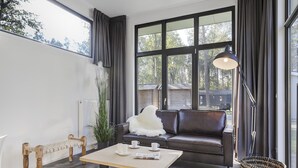A modern living room with a leather sofa, a wooden coffee table, a floor lamp, and large windows with curtains.