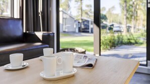 A wooden table with a newspaper, a white pitcher, and two white cups with saucers.