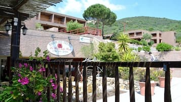 Ein Restaurant mit Terrassensitzgelegenheiten, einer steinernen Fassade und Blick auf einen Hügel.