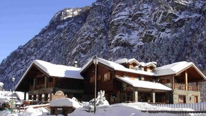 Un chalet en bois doté de plusieurs balcons et d’un toit enneigé, situé dans un décor montagneux.