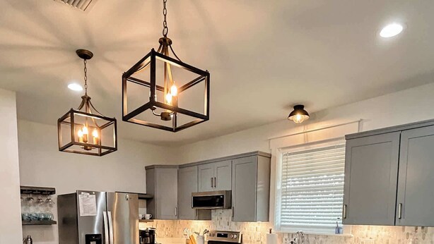 A modern kitchen with grey cabinets, a white marble countertop, and stainless steel appliances. There are pendant lights above the island and a trash bin to the right. - Bay Views, Short beach walk, 3/2, Community Pool (Port St. Joe)