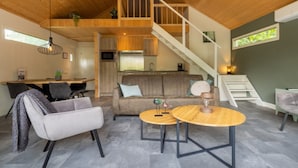Un interior moderno con techo de madera, una escalera, cocina y un área de descanso con sofá y dos mesas redondas.