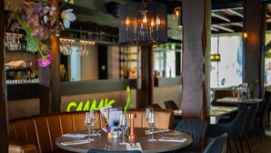 Un interior de restaurante con mesas redondas, sillas oscuras y una barra al fondo.