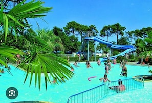 A swimming pool with a water slide, surrounded by palm trees and clear skies.