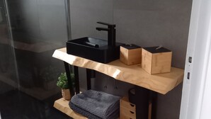 Een moderne badkamer met een zwarte wastafel, houten planken en een kleine plant.