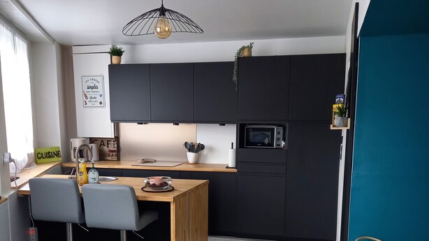 Een moderne keuken met donkere kasten, een houten eiland, twee barkrukken, een magnetron en een hangende lamp.