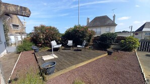 Een houten terras met buitenmeubels, omgeven door grind en beplanting.