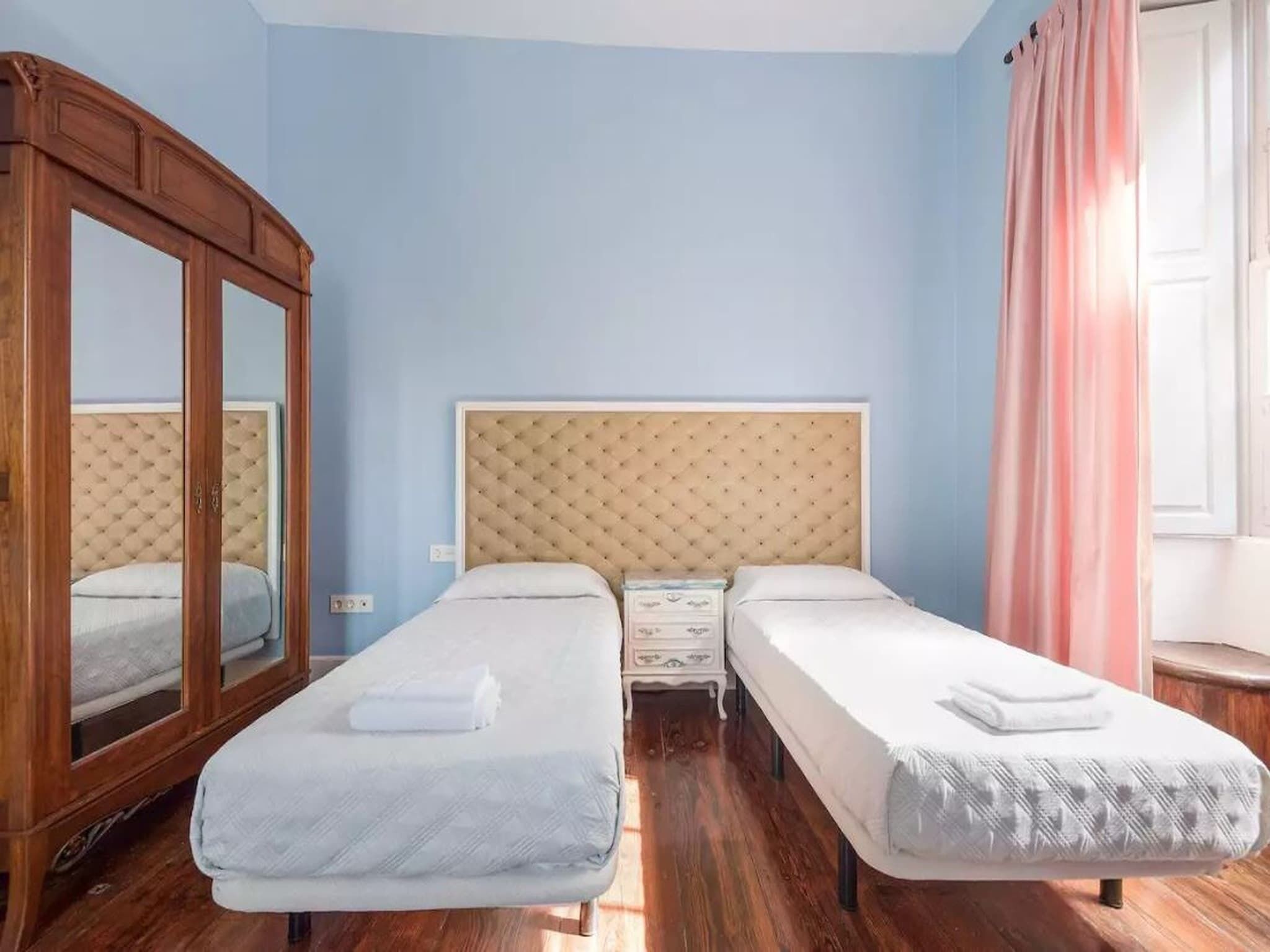 A double room with two beds, a wooden wardrobe, and a mirror.