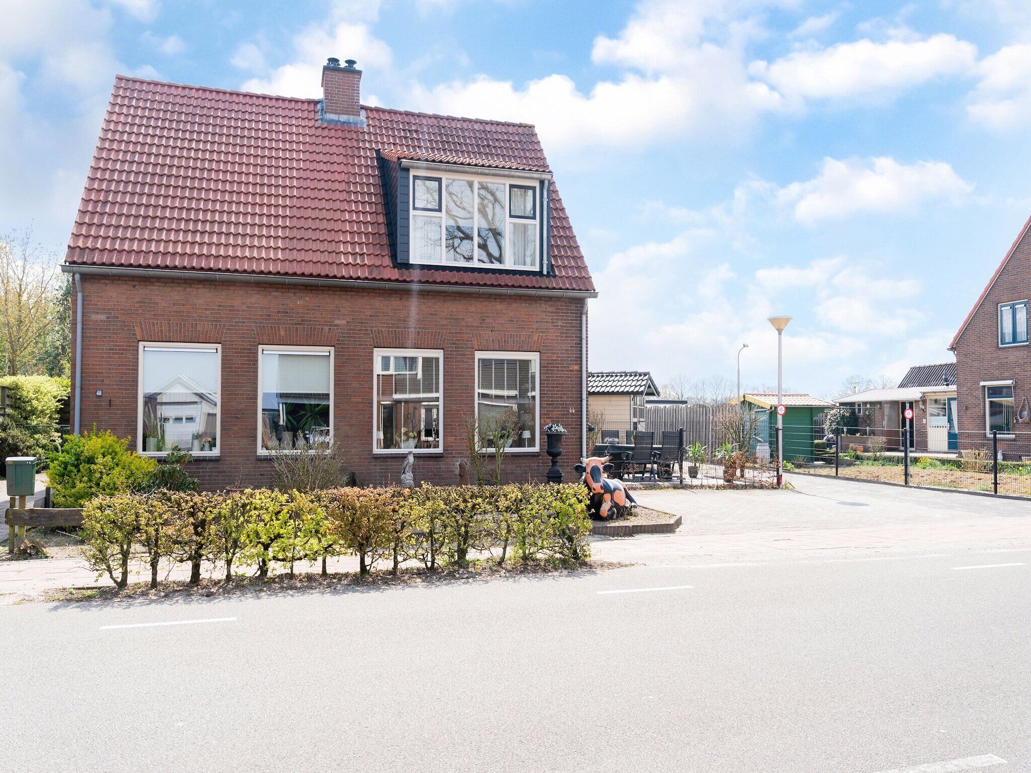 Een gebouw van baksteen met een rood pannendak, meerdere ramen en een kleine tuin met struiken.