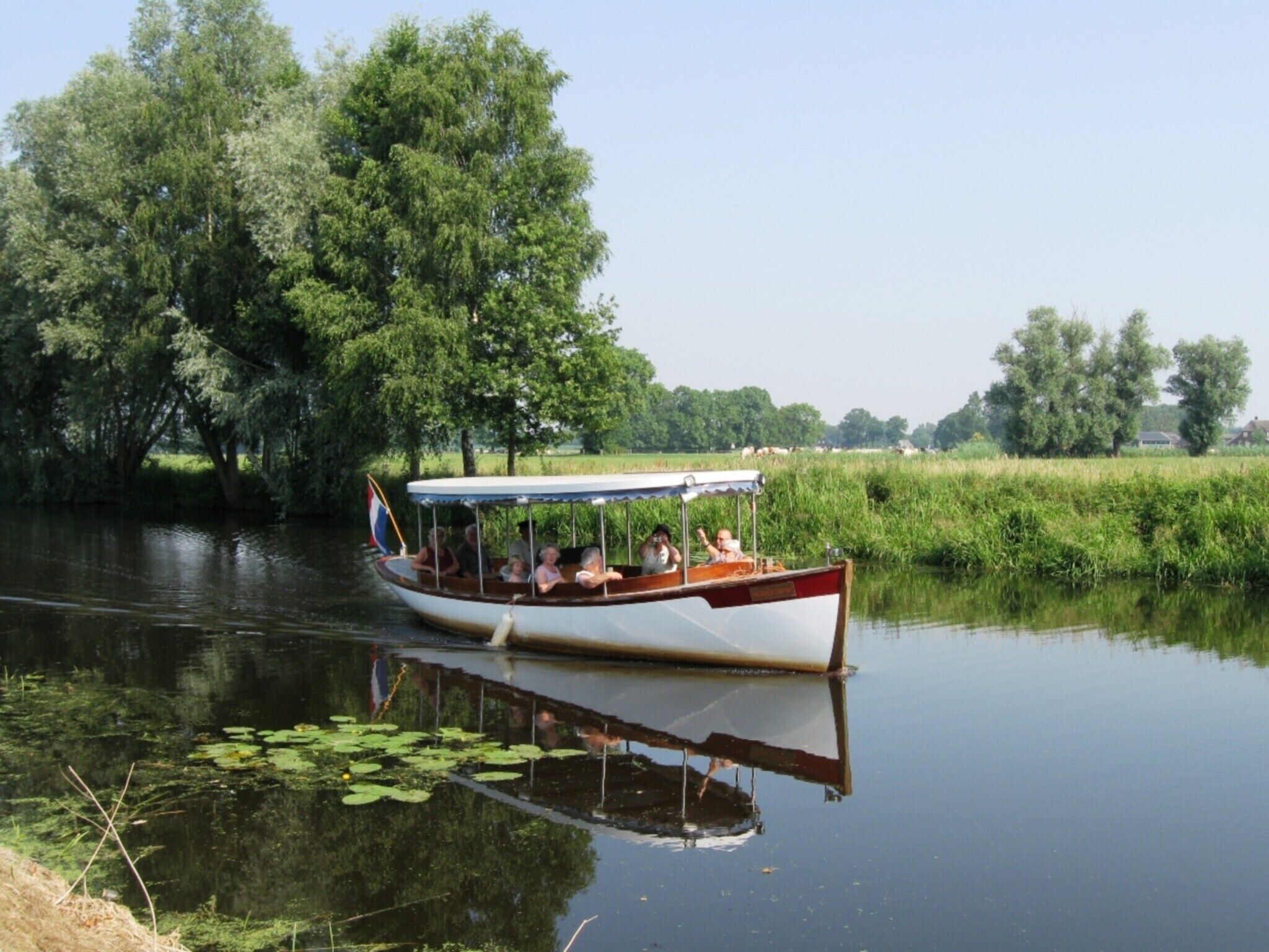 Une péniche remplie de passagers, entourée d’une végétation luxuriante et d’une eau calme.
