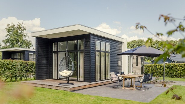 A modern house with a patio area featuring a hanging chair, a table with chairs, and a large umbrella. - Modern Bungalow with Garden in Twente (Rijssen)