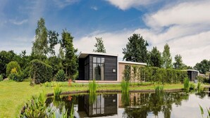 A modern house with a large glass window, surrounded by a pond and greenery. - Modern Bungalow with Garden in Twente (Rijssen)