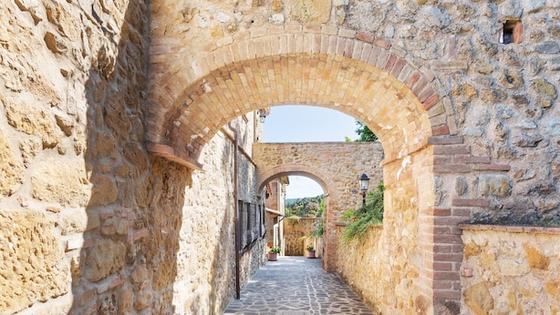 Un étroit sentier de pierre bordé de vieux murs de pierre et surmonté d’un passage en arc de cercle.