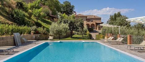 A rectangular swimming pool with clear blue water, surrounded by lounge chairs and a pergola.