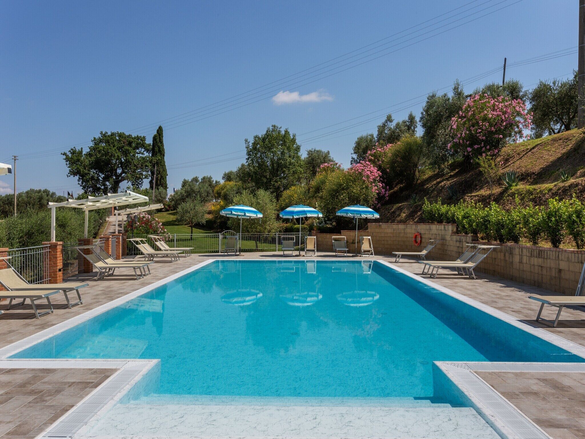 Ein rechteckiger Swimmingpool mit klarem, blauem Wasser, umgeben von Liegestühlen und Sonnenschirmen.