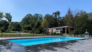 Een rechthoekig zwembad met helderblauw water, omringd door een geplaveid terras.
