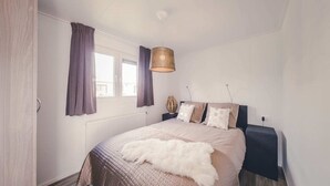 Een slaapkamer met een bed, een raam met gordijnen, een hanglamp en een radiator.