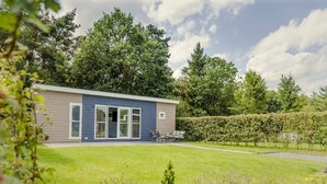 Een modern, gelijkvloers gebouw met een plat dak, grote schuifdeuren en een klein terras met buitenmeubilair.