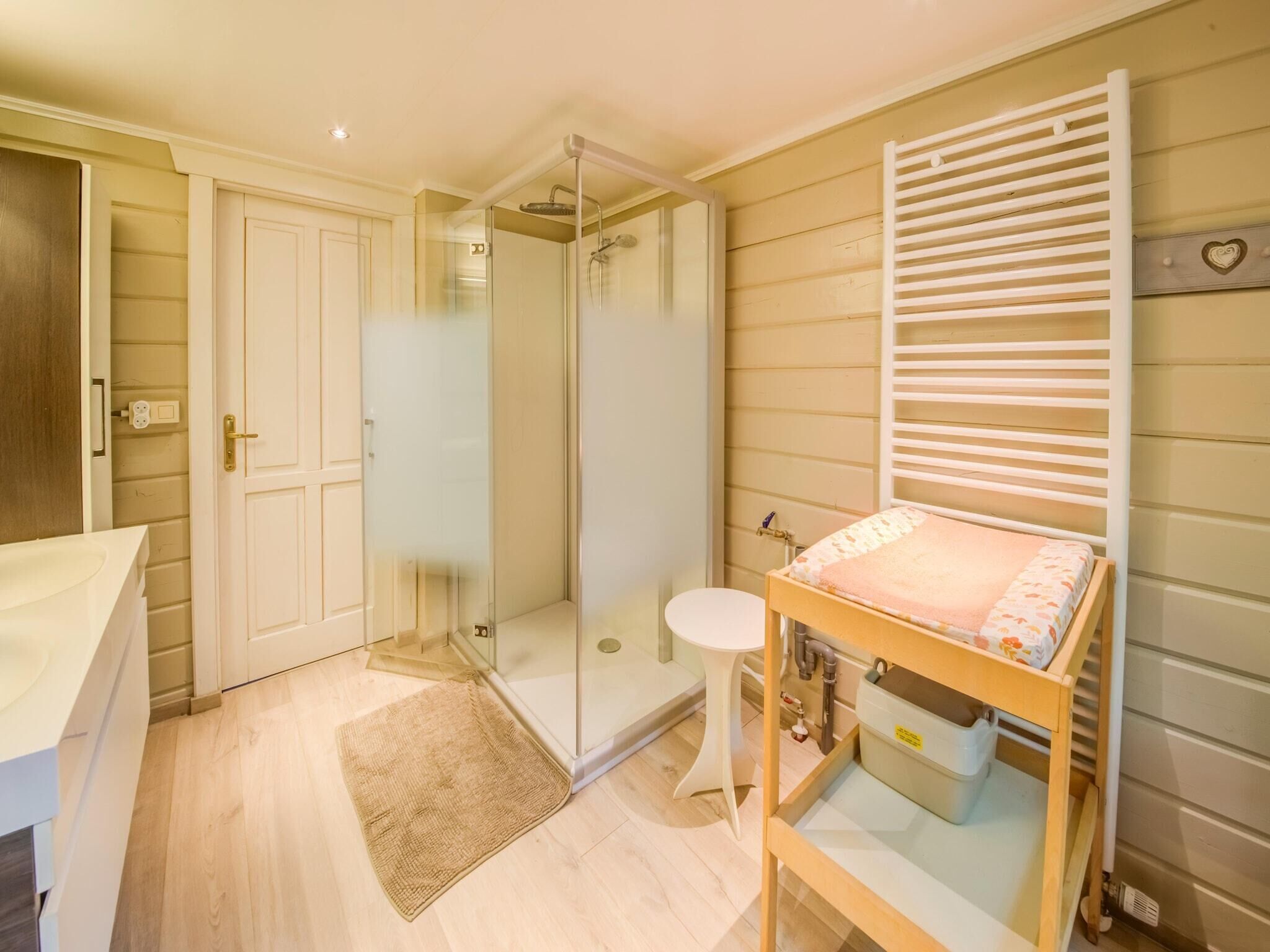 Ein Schlafzimmer mit einer Glasdusche, einem hölzernen Bett, einem Nachttisch und einer weißen Tür.
