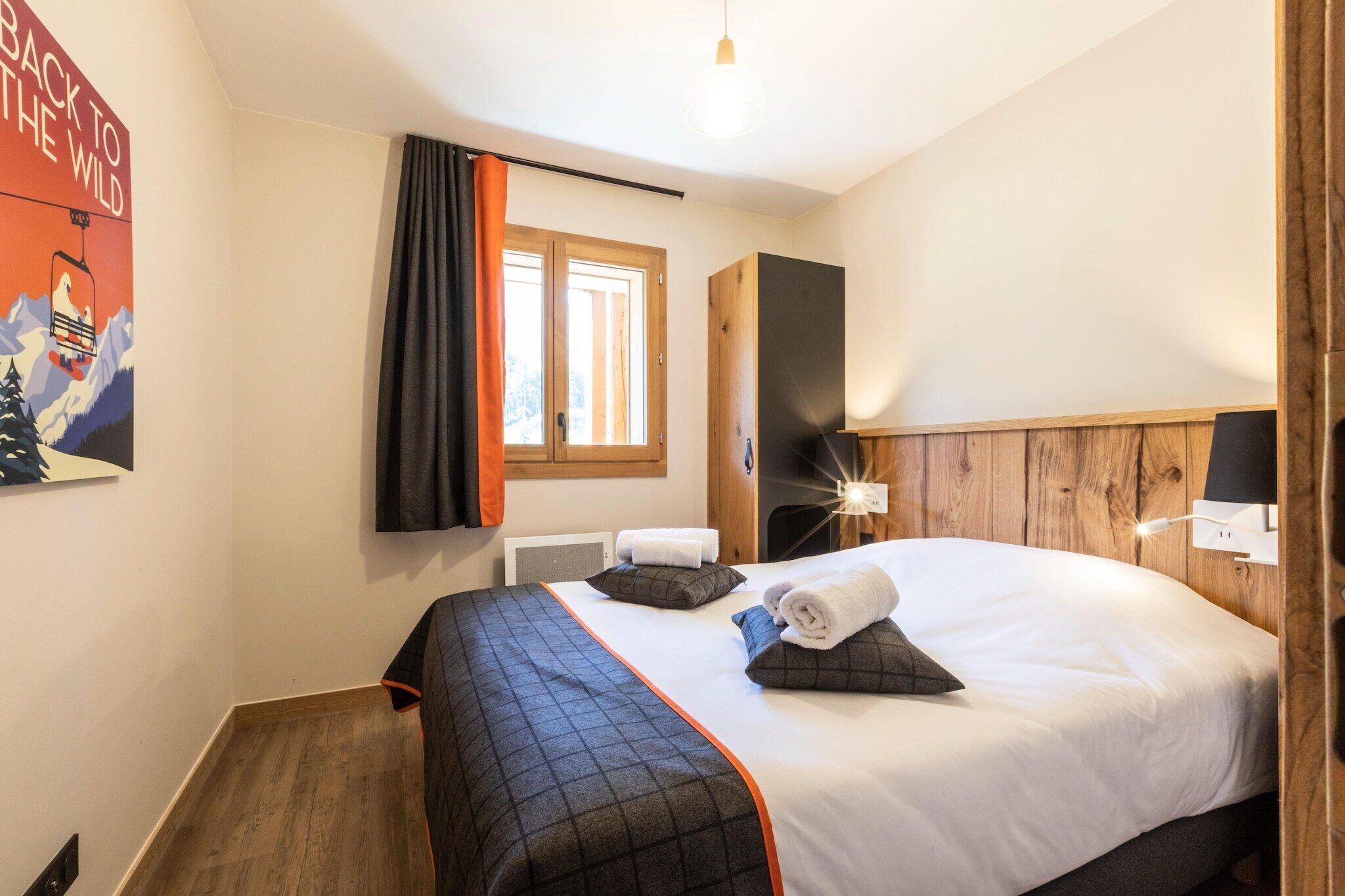 Une chambre d’hôtel avec un grand lit, une tête de lit en bois, une fenêtre avec des rideaux et une affiche accrochée au mur.