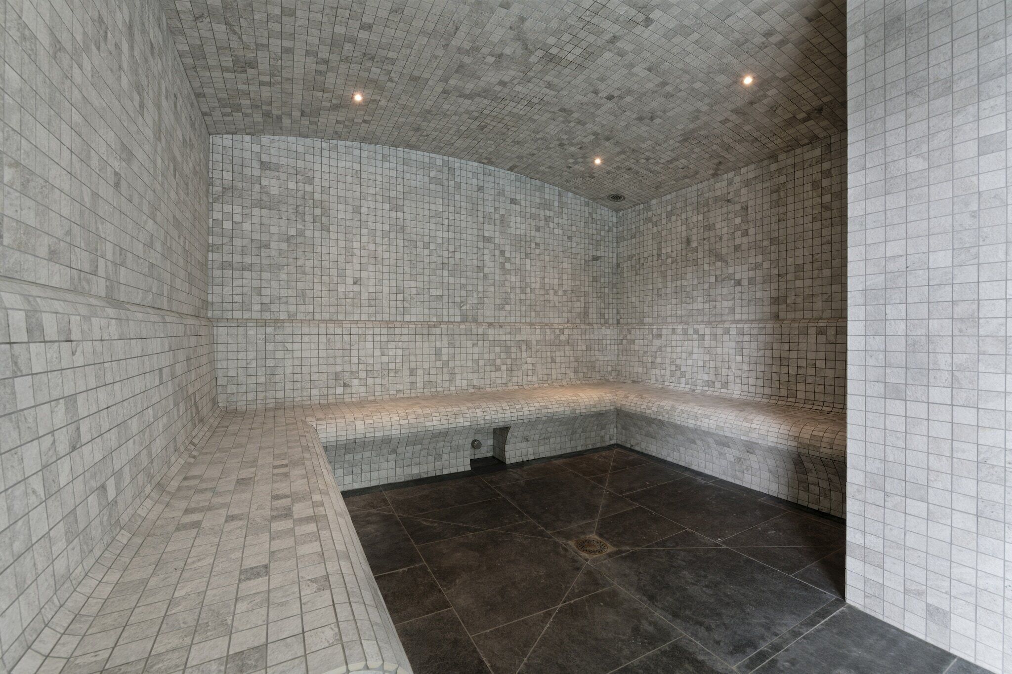 Um espaço de spa moderno com paredes e chão revestidos de azulejos, um banco e uma pia pequena.