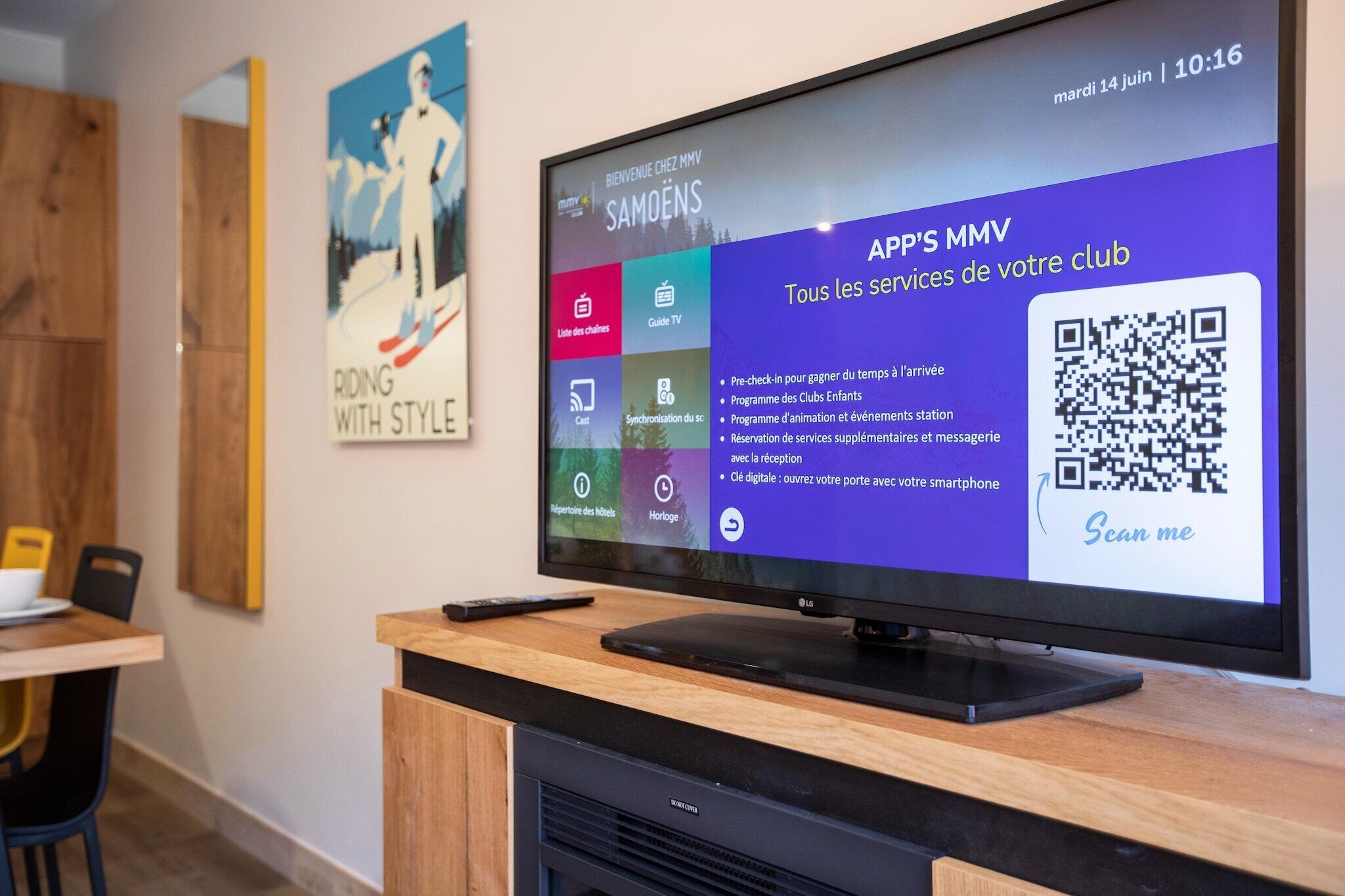 A hotel reception area with a digital screen displaying information about the club's services, a poster on the wall, and a wooden counter with a remote control.