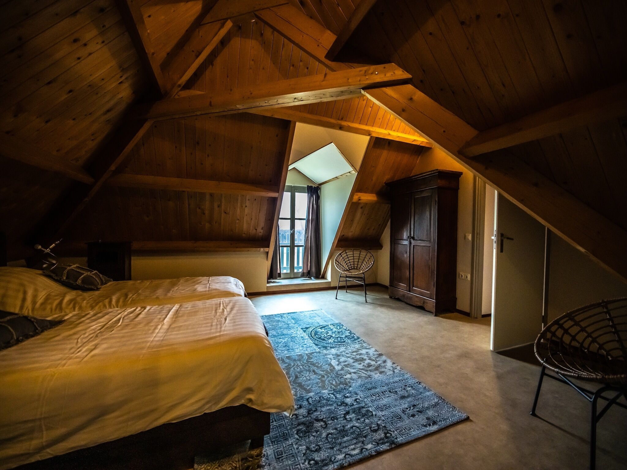 Une chambre mansardée chaleureuse avec un plafond en pente, un grand lit, une armoire et une chaise.