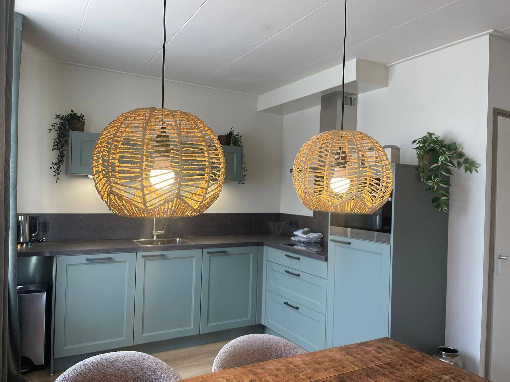 Una cocina moderna con armarios azul claro, una mesa de comedor de madera y dos grandes lámparas colgantes tejidas.