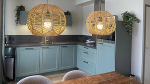 A modern kitchen with light blue cabinets, a wooden dining table, and two large woven pendant lights. - Stay at Oranjezon Dunes (Vrouwenpolder)