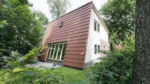 A two-story house with a brown shingle roof, large windows, and a garden with various plants. - Modern Villa Near Veluwe (Hoenderloo)